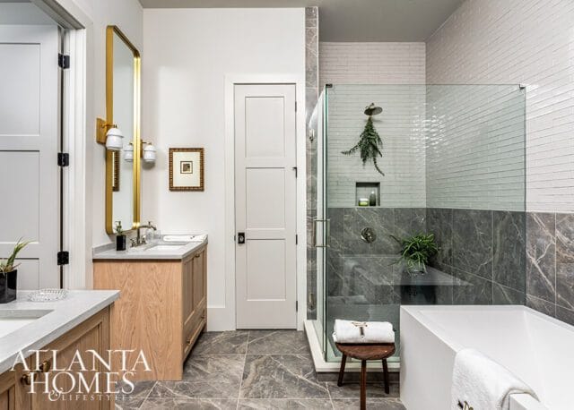 Modern bathroom with wood vanity, gold mirror, marble tile, and glass shower enclosure.