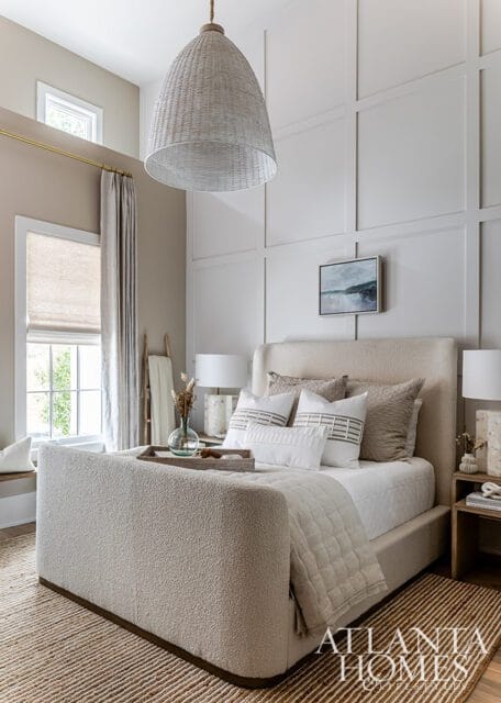 Bedroom with textured headboard, neutral bedding, woven pendant light, and paneled wall.