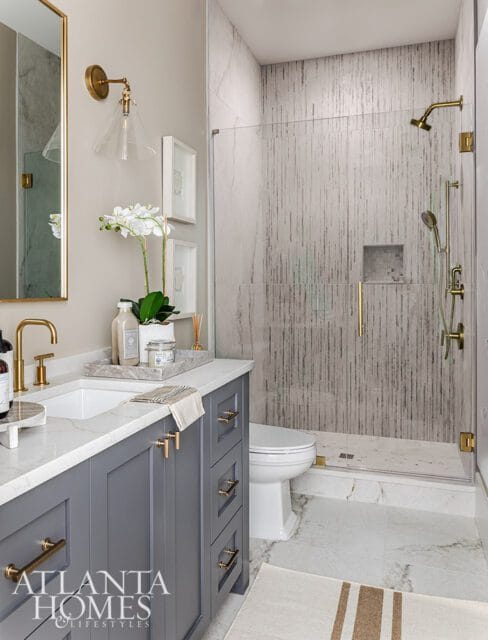 Gray vanity with marble countertop and gold hardware, glass shower with textured tile, and gold