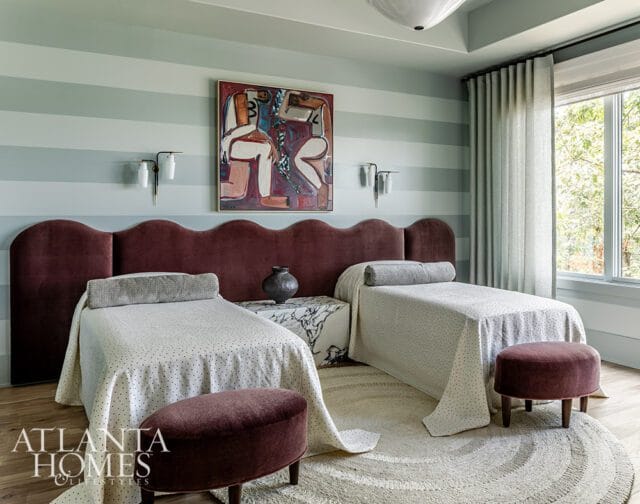 Bedroom with two twin beds, burgundy scalloped headboard, striped walls, and abstract art.