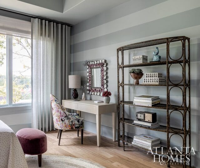 Bedroom with striped walls, light wood desk, floral chair, and metal shelving unit.