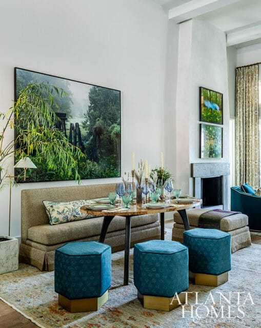 Dining area with a large landscape painting, round table set for dinner, and teal ottomans.