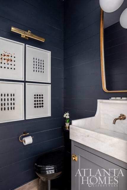 Dark blue shiplap bathroom with black toilet, marble sink, and framed botanical prints