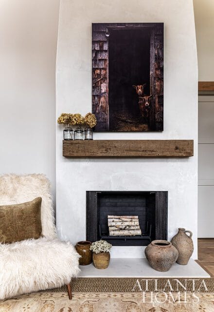 Living room with fireplace, rustic art of goats, and textured chair.