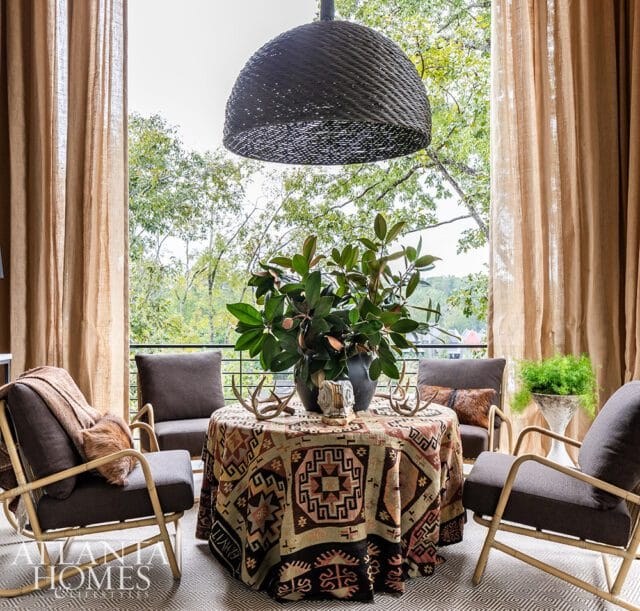 Sitting area with patterned tablecloth, wicker pendant light, and chairs overlooking trees.