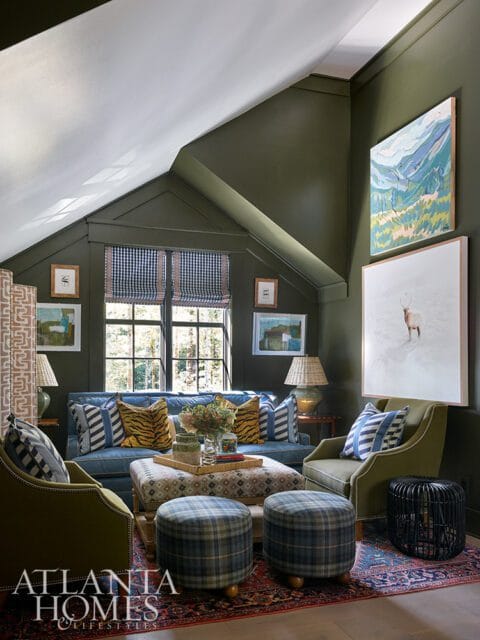 Living room with olive green walls, blue sofa, plaid ottomans, and artwork