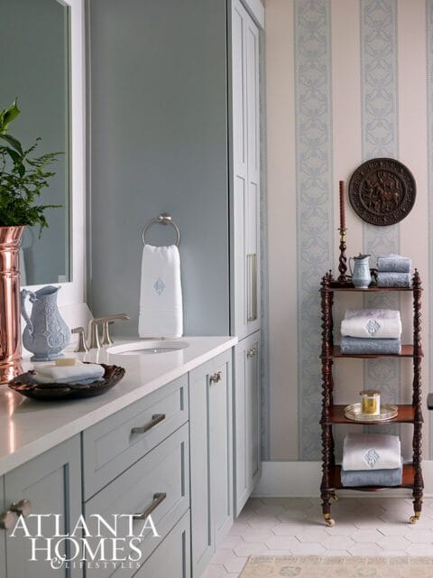 Light blue vanity with white countertop, silver faucet, and white towels. Striped wallpaper with