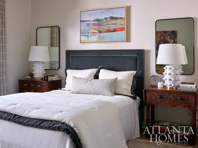 Bedroom with dark gray upholstered headboard, white bedding, and abstract art above the bed.