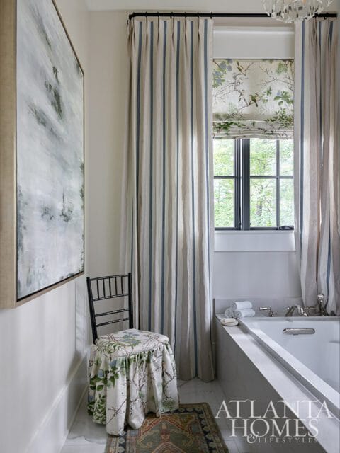 Bathroom with striped curtains, floral Roman shade, and a chair with a floral skirt.