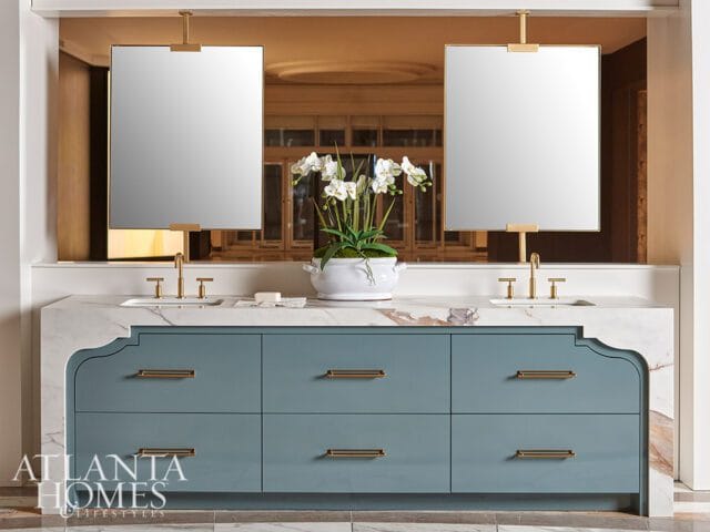 Blue vanity with marble countertop, brass hardware, and two hanging mirrors.