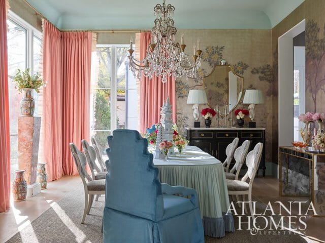 Elegant dining room with a crystal chandelier, pale blue ceiling, coral drapes, and a table set with a light blue tablecloth and chairs upholstered in a patterned fabric.