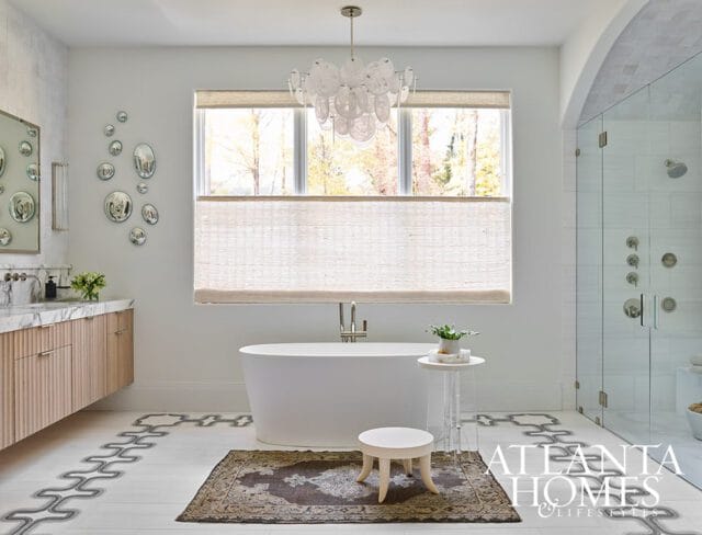 Modern bathroom with freestanding tub, glass-enclosed shower, marble vanity with fluted wood cabinets, and decorative floor tile.