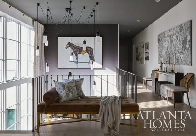 Hallway landing with a brown velvet chaise lounge, patterned pillows, and a painting of a horse above a dark gray wall. A multi-light pendant hangs overhead.