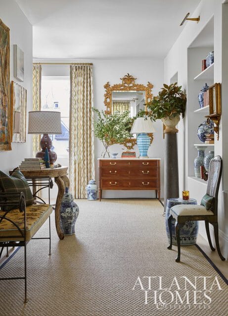 Hallway with a wooden dresser, ornate gold mirror, blue and white porcelain vases, patterned curtains, and a bench with plaid cushions.
