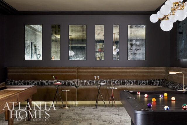 Dark room with a pool table, built-in velvet banquette seating with patterned pillows, and a wall of five distressed mirrors above the seating.