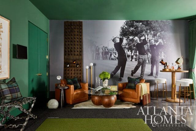 Living room with green walls, a large black and white mural of golfers, two leather armchairs, a glass coffee table, and a bar area with stools.
