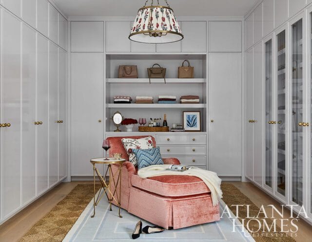 Walk-in closet with floor-to-ceiling white cabinetry, a pink velvet chaise lounge, and a floral pendant light.