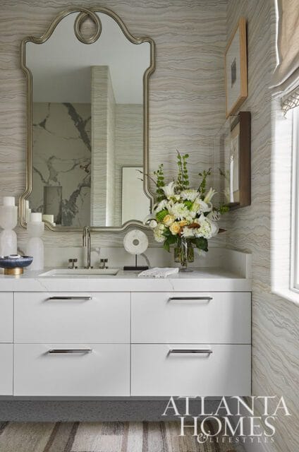 Modern white bathroom vanity with marble countertop, polished nickel hardware, and a large ornate mirror above. A floral arrangement sits on the counter.