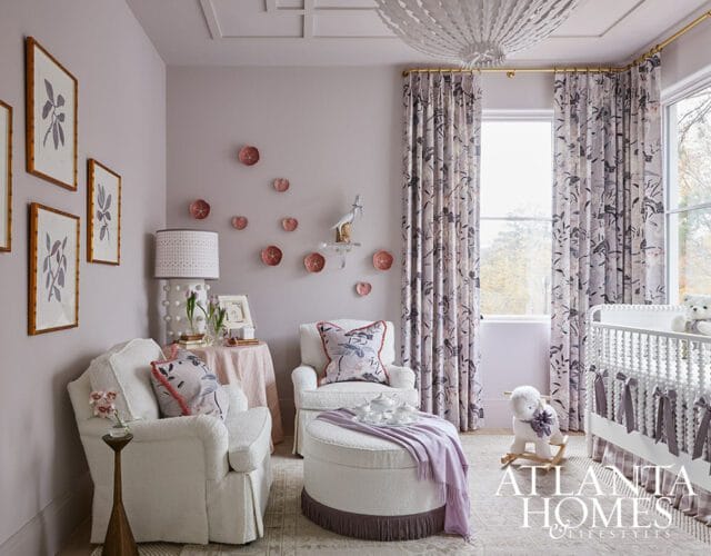 Nursery with lavender walls, white boucle armchairs, ottoman, floral curtains, crib with lavender bows, and framed botanical prints.