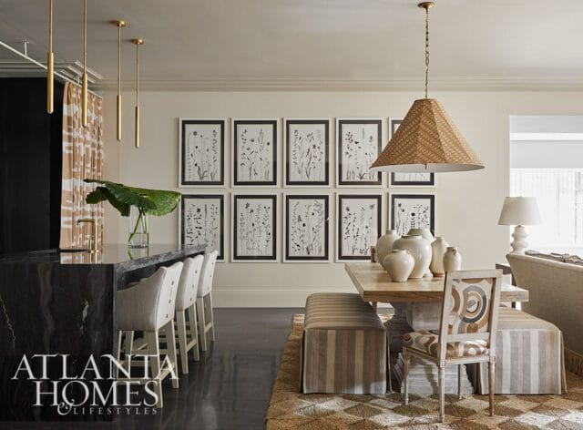 Modern dining room with a black marble island, upholstered bar stools, a wooden dining table with ceramic vases, and a gallery wall of botanical prints.