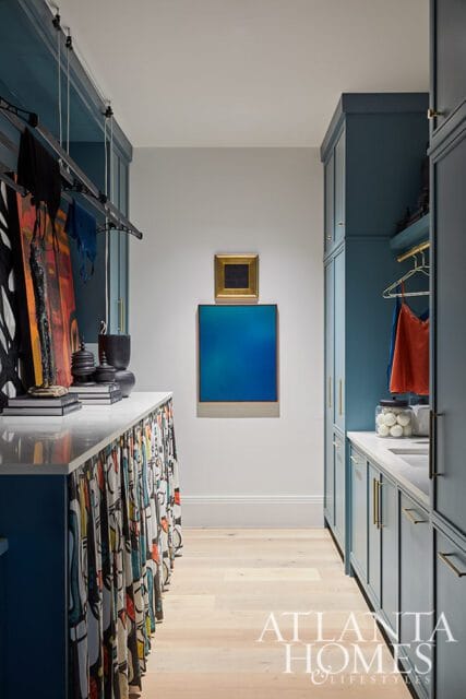 Walk-in closet with teal cabinetry, white countertops, and a hanging rack with artwork and clothing. A blue abstract painting hangs on the wall.