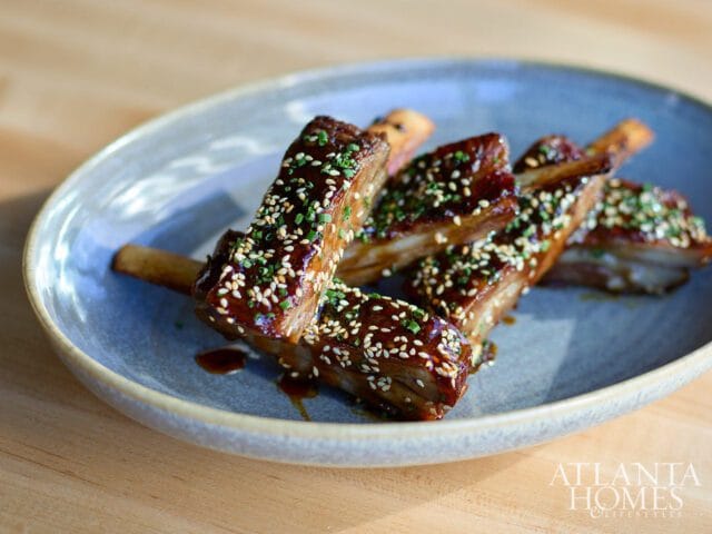 Glazed ribs sprinkled with sesame seeds and chopped chives on a blue-grey oval plate.