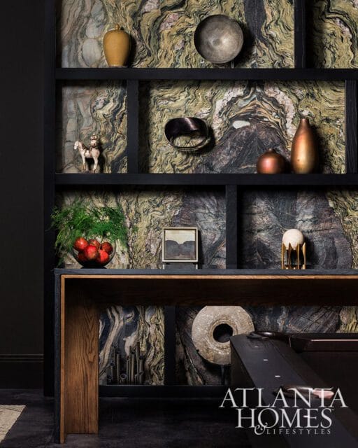 Dark wood console table against a wall with dramatic green and black marble wallpaper, displaying various decorative objects and a black shelving unit.