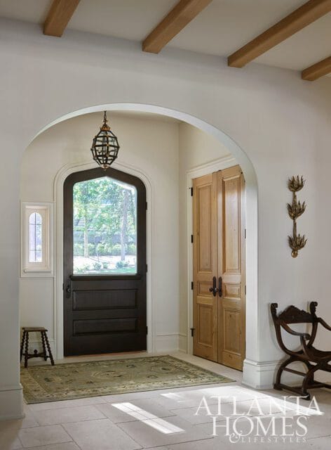 Entryway with arched doorway, dark wood door with glass, double wood doors, and stone tile floor.