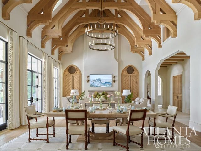 Great room with vaulted wood-beamed ceiling, large windows with cream curtains, and a dining table set for a meal.