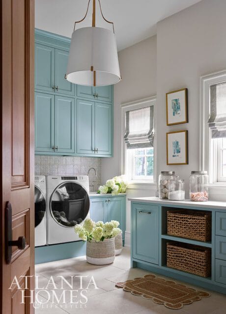 Light blue laundry room with white washer and dryer, light gray tile backsplash, white countertops, and woven baskets on shelves.