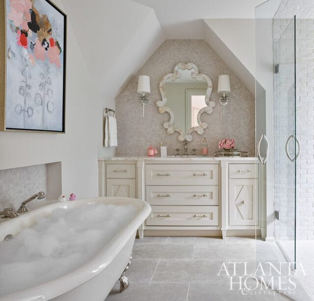 Cream bathroom with clawfoot tub filled with bubbles, ornate mirror above vanity, and glass-enclosed shower with white subway tile