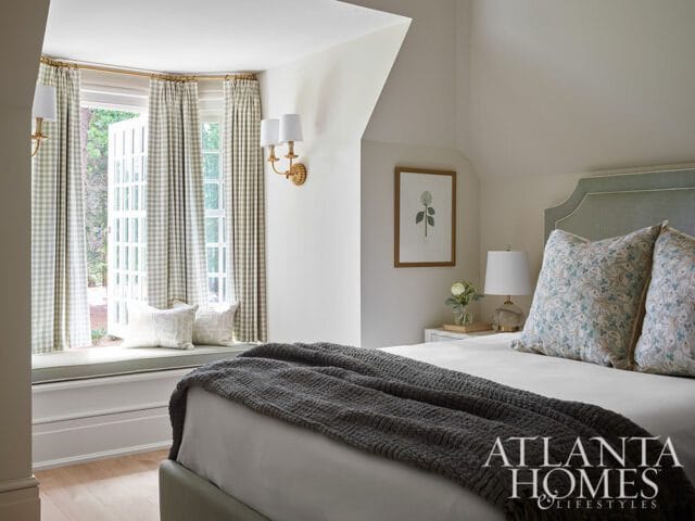 Bedroom with a bay window featuring green gingham curtains and a window seat, a bed with patterned pillows and a dark gray throw, and a light blue upholstered headboard.