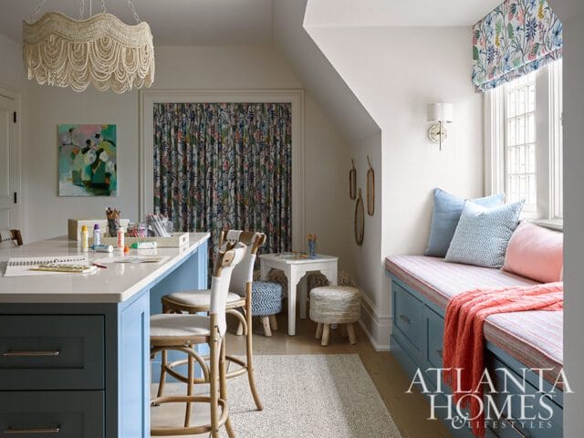 Craft room with a large island, blue cabinetry, and a window seat with blue and pink cushions. A beaded chandelier hangs overhead.