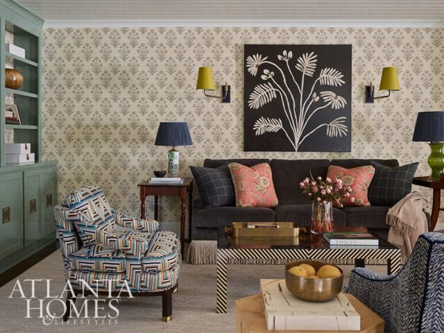 Living room with patterned wallpaper, a dark gray sofa with coral and plaid pillows, a colorful armchair, and a black and white striped coffee table.