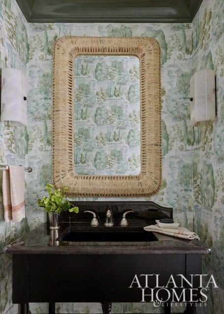 Powder room with scenic toile wallpaper, a black granite vanity with a silver sink and faucet, and a rectangular mirror with a woven rope frame.