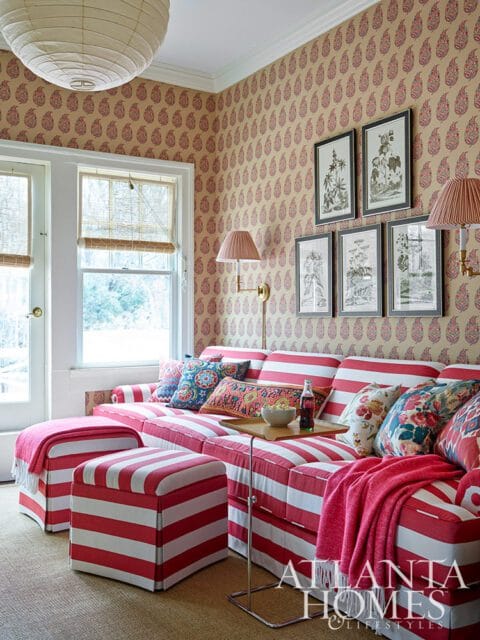 Living room with red and white striped sectional sofa and ottomans, patterned wallpaper, and framed botanical prints.