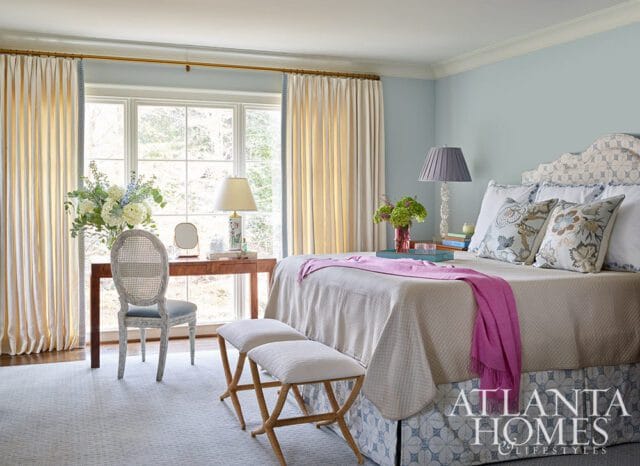 Light blue bedroom with a queen-size bed, patterned headboard, cream bedding, pink throw, and a wooden desk with a cane-back chair.