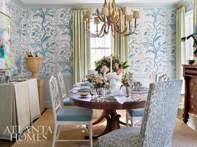 Dining room with blue and white Chinoiserie wallpaper, a round wooden table set for a meal, and light green drapes.