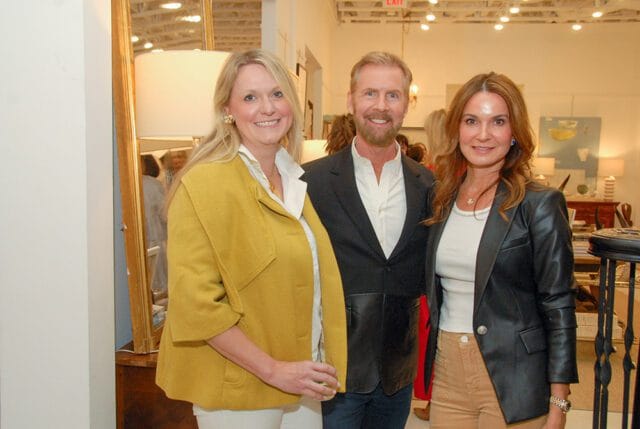 Three people posing for a photo indoors. A woman in a yellow jacket smiles, a man in a dark blazer smiles, and a woman in a black leather jacket smiles.