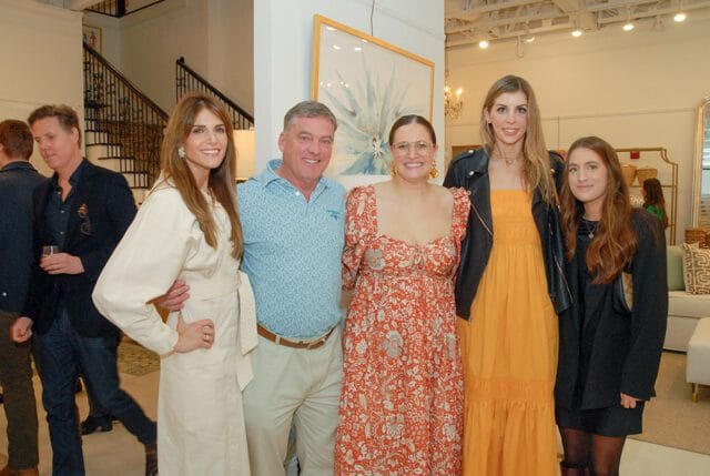 Five people pose for a photo indoors, with a staircase and artwork visible in the background.