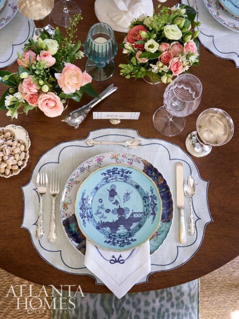 A formal dining table setting with blue and white patterned plates, pink floral arrangements, silver cutlery, and a name card that reads 'Elsie'.