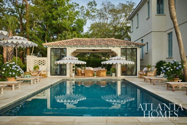 Luxury backyard with a swimming pool, covered patio with wicker furniture, and a stucco house with blue-trimmed windows.