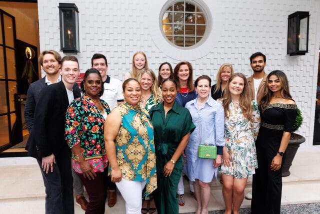 Group of people posing for a photo in front of a white textured wall with a circular window.