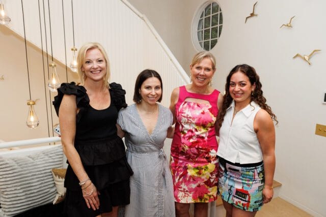 Four women pose for a photo in front of a staircase with decorative bird sculptures on the wall.