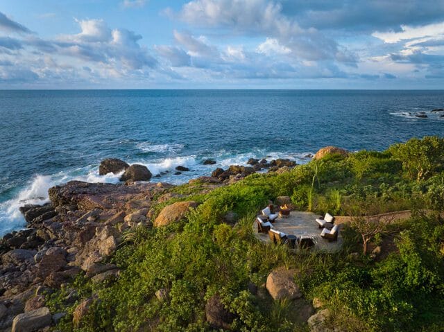 Outdoor seating area with chairs and a fire pit on a rocky coastline overlooking the ocean