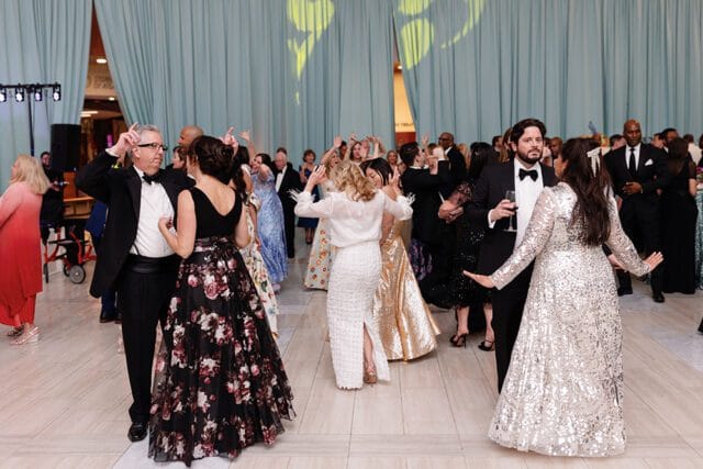 People in formal attire dancing at an event with light blue curtains in the background and yellow lighting projected on them.