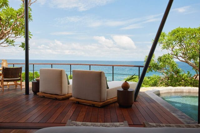 Deck with two white lounge chairs and a small plunge pool overlooking the ocean under a blue sky with clouds.