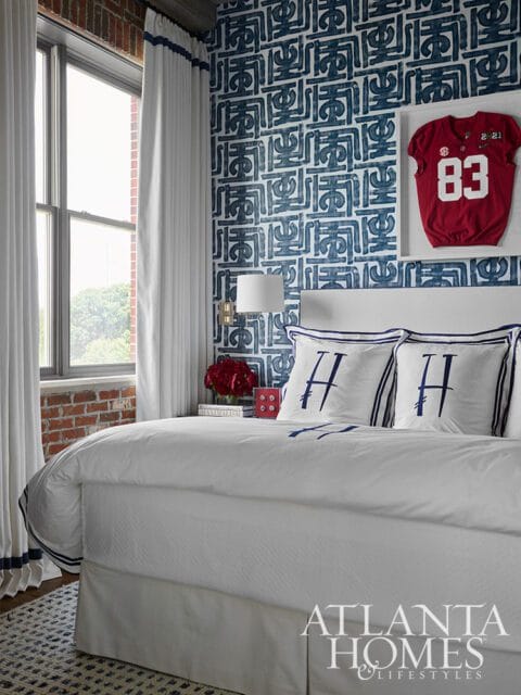 Bedroom with white bedding, navy and white patterned wallpaper, and a framed red football jersey with the number 83.