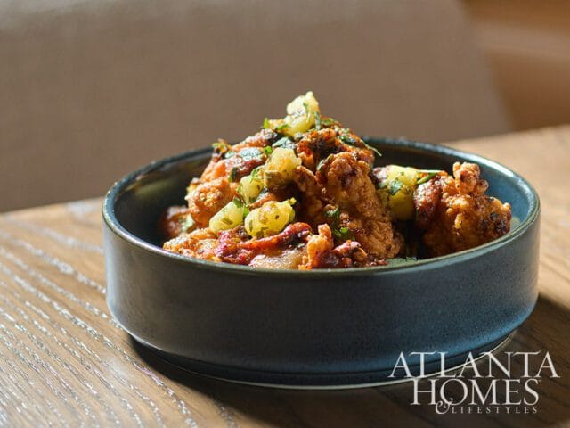 Bowl of fried food topped with herbs and sauce, with Atlanta Homes & Lifestyles logo in the corner.