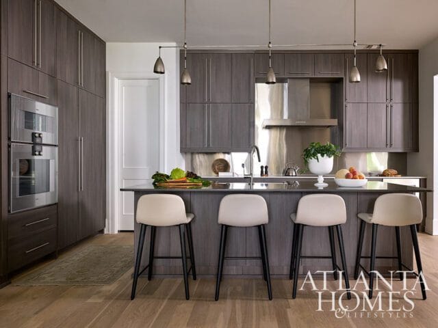 Modern kitchen with dark wood cabinetry, stainless steel appliances, a dark island with four cream bar stools, and pendant lighting.